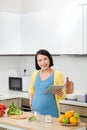 Smiling young pregnant woman using digital tablet while cooking in kitchen Royalty Free Stock Photo