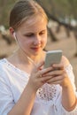 Smiling young pretty girl walking outdoors listening to music with earphones using mobile phone chatting Royalty Free Stock Photo