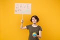 Smiling young protesting woman hold protest sign broadsheet placard on stick Earth world globe isolated on yellow