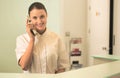 Smiling young receptionist talking on phone at checkout counter