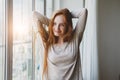 Smiling young red haired girl waking up, stretching, raising hands, happy new morning, sunrise light Royalty Free Stock Photo