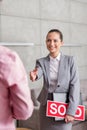 Smiling young saleswoman holding sold placard and document while greeting man in apartment