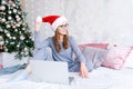 Smiling young Santa girl in cozy clothes in Christmas hat using laptop computer Royalty Free Stock Photo