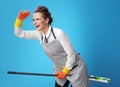 Smiling young scrubwoman using mop as broomstick on blue