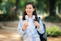 Smiling young student with headphones around her neck using a smartphone in a sun-drenched park