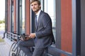 Smiling young stylish man using mobile phone while drinking coffee outdoors with bicycle. Royalty Free Stock Photo