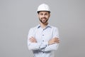 Smiling young unshaven business man in light shirt protective construction helmet isolated on grey background