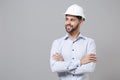 Smiling young unshaven business man in light shirt protective construction helmet isolated on grey wall background