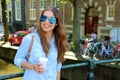 Smiling young urban woman with aviator sunglasses holding coffee outdoor in Amsterdam centre, Netherlands, Europe