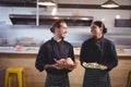 Smiling young wait staff looking at each other while holding fresh food in coffee shop Royalty Free Stock Photo