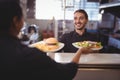 Smiling young waiter giving food to waitress at counter Royalty Free Stock Photo