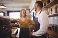 Smiling young waiter and waitress standing by espresso maker