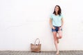 Smiling young woman with bag leaning against white wall Royalty Free Stock Photo