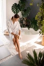 Smiling young woman in bathrobe dry brushing her legs with a natural wooden brush while sitting on the side of a bathtub Royalty Free Stock Photo