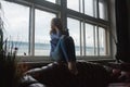 Smiling young woman in blue striped shirt, ripped jeans sitting on windowsill Royalty Free Stock Photo