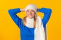 Smiling young woman in blue sweater posing in white hat and scarf over yellow background Royalty Free Stock Photo