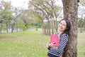 Smiling young woman with book standing lean against trunk tree in summer park outdoor Royalty Free Stock Photo