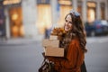 smiling young woman in brown trench coat with parcels