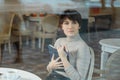 Smiling young woman in a cafe taking notes in notepad during coffee break, view through window glass Royalty Free Stock Photo