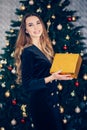 Smiling young woman with christmas present box near christmas tree in a black dress Royalty Free Stock Photo