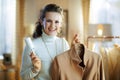 Smiling young woman cleaning coat on hanger with lint roller