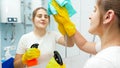 Smiling young woman cleaning and washing bathroom mirror with chemical detergent spray. Housewife doing home cleanup and Royalty Free Stock Photo