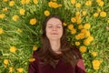 Smiling young woman with closed eyes relaxing on a meadow with many dandelions in the spring sun. Top down view. Royalty Free Stock Photo