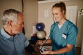 Smiling young woman doctor checking senior patient blood pressure using instrument and stethoscope in clinic Royalty Free Stock Photo