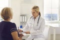 Smiling young woman doctor writing complaints of elderly woman patient Royalty Free Stock Photo