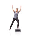 Reaching her fitness goals. A smiling young woman doing aerobics on an aerobic step against a white background - K-step.