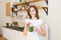 Smiling young woman drinking green smoothie juice in kitchen. Royalty Free Stock Photo