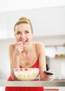 Smiling young woman eating popcorn and watching tv in kitchen Royalty Free Stock Photo