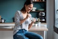 Smiling young woman eating yogurt while sitting on stool in the kitchen at home Royalty Free Stock Photo