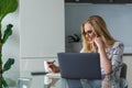 smiling young woman in eyeglasses using laptop and taking notes while working