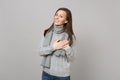 Smiling young woman in gray sweater, scarf holding hands folded on heart on grey wall background. Healthy
