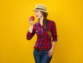 Smiling young woman grower on yellow background eating an apple