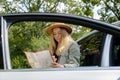 Smiling young woman in hat stoped on road to check the route on travel map. Local solo travel on weekends concept Royalty Free Stock Photo