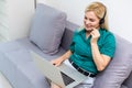 Smiling young woman with headphones and laptop on the sofa. Working from home in quarantine lockdown. Social distancing