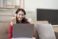 Smiling young woman with headphones using laptop in livingroom. Female studying at home. Young woman wearing headphones Royalty Free Stock Photo