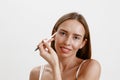 Smiling young woman with healthy skin combing her eyebrows with brush over white studio background Royalty Free Stock Photo