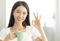 Smiling young woman holding coffee cup  and showing ok gesture Royalty Free Stock Photo