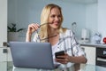 smiling young woman holding eyeglasses and looking away while working with digital devices