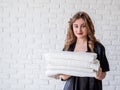 Smiling young woman holding a pile of towels on white bricks background Royalty Free Stock Photo