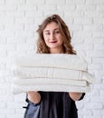 Smiling young woman holding a pile of towels on white bricks background Royalty Free Stock Photo