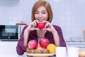 Smiling young woman holding red heart shape in her hand with fruit and fresh milk in breakfast at home looking at camera Royalty Free Stock Photo