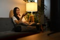 Smiling young woman holding remote control, watching TV in cozy living room. Entertainment, technology and hobby concept Royalty Free Stock Photo