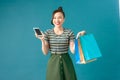 Smiling young woman holding shopping bags, using mobile phone Royalty Free Stock Photo