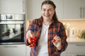 Smiling young woman holding tomato, standing at modern kitchen, chopping vegetables, preparing fresh healthy salad for Royalty Free Stock Photo