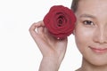 Smiling young woman holding up a red rose next to her ear, studio shot Royalty Free Stock Photo