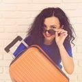 Smiling young woman hugging her orange suitcase. Casual girl is ready to travel. Happy woman in sunglasses dreaming about vacation Royalty Free Stock Photo